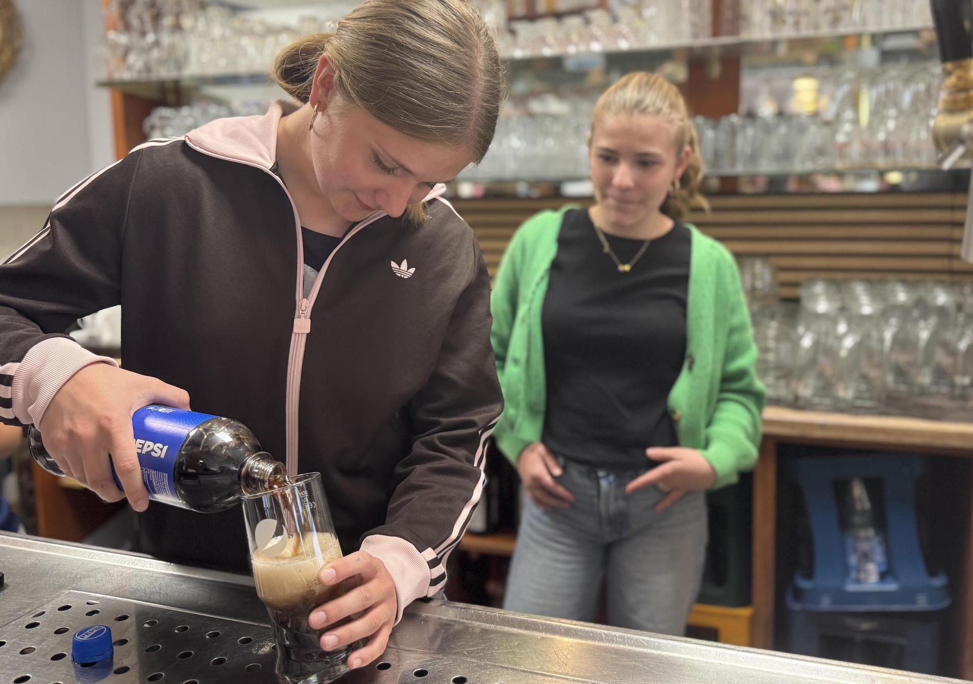 Emilia Schmidt übt sich am Eingießen einer Cola, Marie Hämmerling schaut zu. (Foto: Daniel Große)